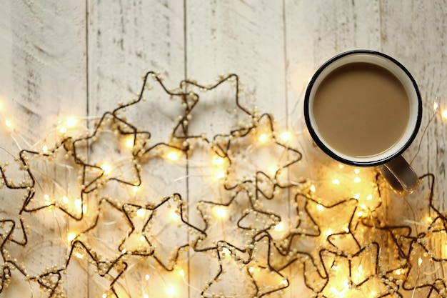 Kaffeetasse und glänzende Girlande in Form der Sterne auf einem hellen schäbigen schicken Hintergrund.