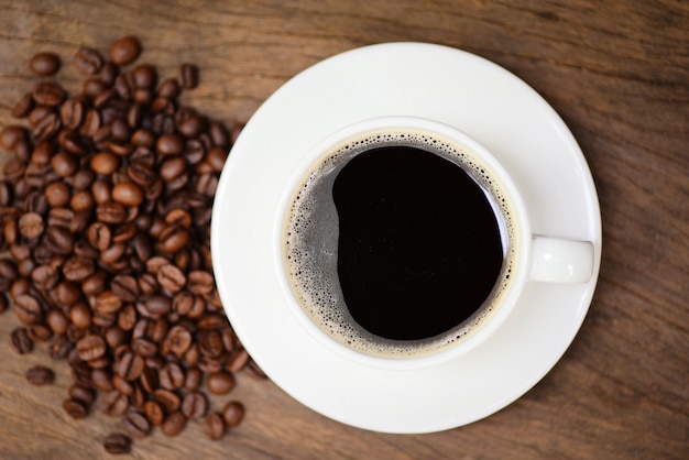 Kaffeetasse und Kaffeebohnen auf Tisch / schwarzer Kaffee im weißen Becher