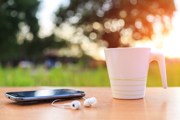 Kaffeetasse und Smartphone auf dem Tisch in der Sonnenuntergangzeit