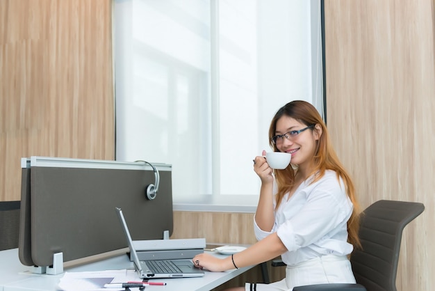 Kaffeezeit der Bürofrau mit Brille im BüroThailändisches Mädchen arbeitet am SchreibtischGeschäftsfrau im weißen Kleid