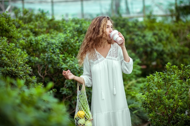 Kaffeezeit. Frau im weißen Kleid mit den Taschen des Gemüses, das Kaffee trinkt