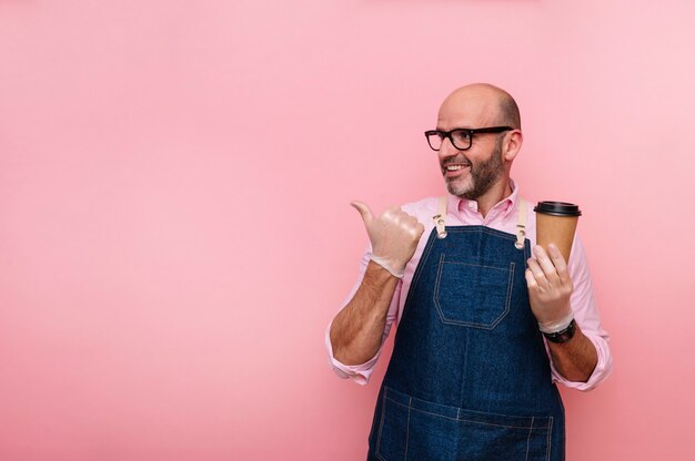 Kahler reifer Mann, der seinen Daumen zeigt und Kaffee im recycelbaren Pappbecher hat