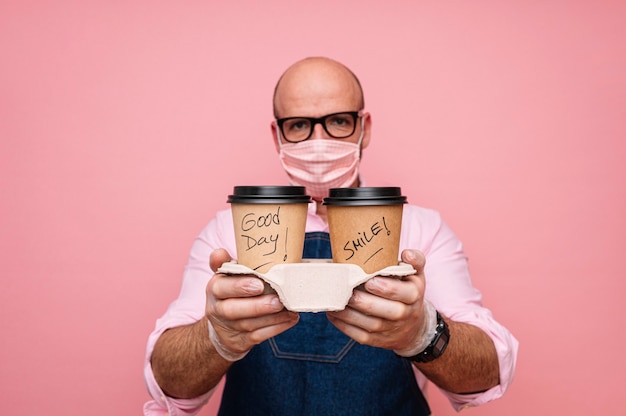 Kahler reifer Mann mit Gesichtsmaske und Kaffee im recycelbaren Pappbecher