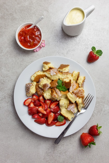 Kaiserschmarren oder Kaiserschmarrn, traditionelles österreichisches oder deutsches süßes Pfannkuchendessert mit frischen Beeren, Erdbeermarmelade oder roter Grutze und Vanillepudding-Sauce