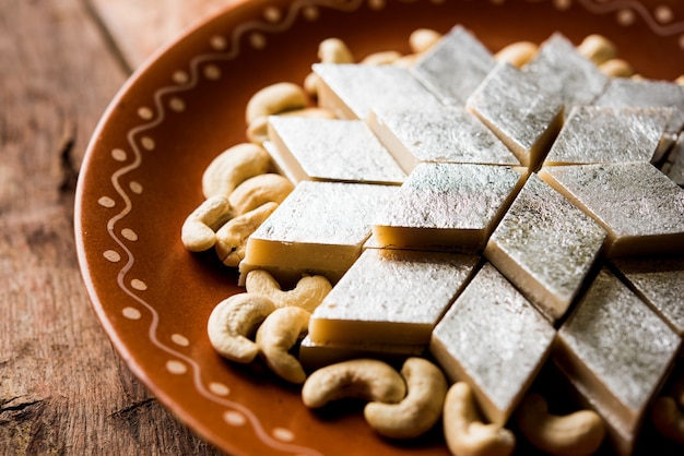 Kaju Katli es un dulce indio con forma de diamante elaborado con azúcar de anacardo y mava, servido en un plato sobre una superficie de mal humor. enfoque selectivo