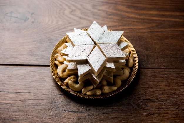 Kaju Katli es un dulce indio con forma de diamante elaborado con azúcar de anacardo y mava, servido en un plato sobre una superficie de mal humor. enfoque selectivo