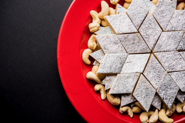 Kaju Katli ist eine indische Süßigkeit in Diamantform, die aus Cashewzucker und Mava hergestellt wird und in einem Teller auf einer stimmungsvollen Oberfläche serviert wird. selektiver Fokus