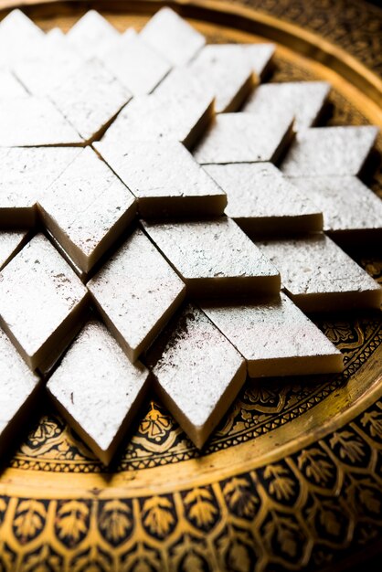 Kaju Katli ist eine indische Süßigkeit in Diamantform, die aus Cashewzucker und Mava hergestellt wird und in einem Teller auf einer stimmungsvollen Oberfläche serviert wird. selektiver Fokus