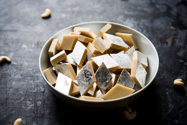 Kaju Katli ist eine indische Süßigkeit in Diamantform, die aus Cashewzucker und Mava hergestellt wird und in einem Teller auf einer stimmungsvollen Oberfläche serviert wird. selektiver Fokus