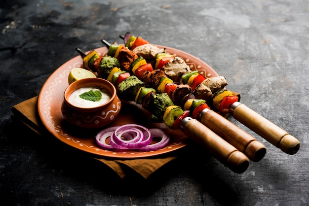 Kakab de frango hariyali ou kebab de malai malai tricolor servido com espetos e molho de iogurte em um prato