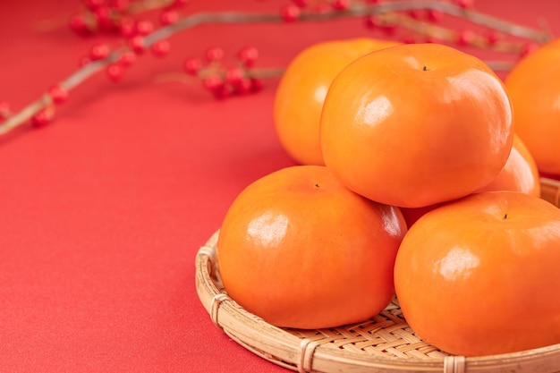 Kaki caqui dulce en rodajas hermosas y frescas aislado sobre fondo de mesa rojo y tamiz de bambú Concepto de diseño de año nuevo lunar chino de cerca