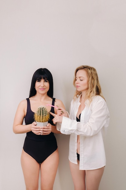 Kaktus-Konzept Unrasierter Körper Ein Mädchen hält einen Kaktus in ihren Händen und das zweite Mädchen hält ein Rasiermesser Symbol für unrasierte Körperteile