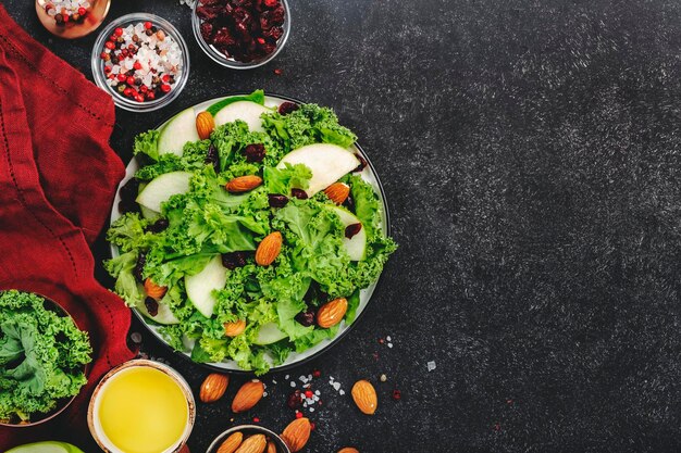 Kale-Salat mit getrockneten Cranberry-Grünäpfeln und Mandeln Vegane gesunde Lebensmittel Draufsicht schwarzer Küchentisch