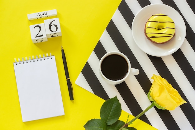 Kalender 26. April Tasse Kaffee, Donut und Rose, Notizblock für Text. Konzept stilvoller Arbeitsplatz