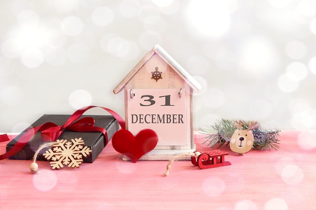 Kalender für den 31. Dezember: dekoratives Haus mit dem Namen des Monats in Englisch, Nummer 31, Geschenkverpackung, mit rotem Band gebunden, rotes Herz, Neujahrsspielzeug, Bokeh.