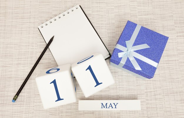 Kalender mit trendigen blauen Text und Zahlen für den 11. Mai und ein Geschenk in einer Box.