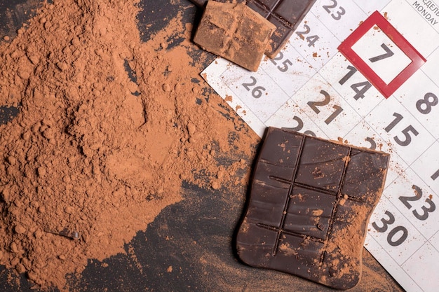 Kalender Nahaufnahme mit gebrochenem Schokoriegel und Kakaopulver Weltschokoladentag 7. juli