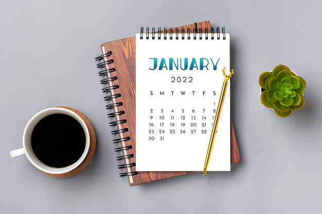 Kalender öffnen Januar 2022 Tasse Kaffee Stift auf grauem Hintergrund