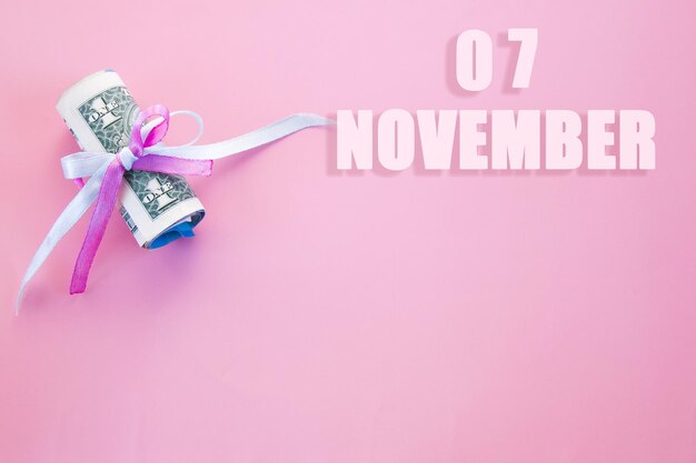 Kalenderdatum auf rosafarbenem Hintergrund mit aufgerollten Dollarscheinen, die von rosafarbenem und blauem Band mit Kopierbereich festgehalten werden Der 7. November ist der siebte Tag des Monats