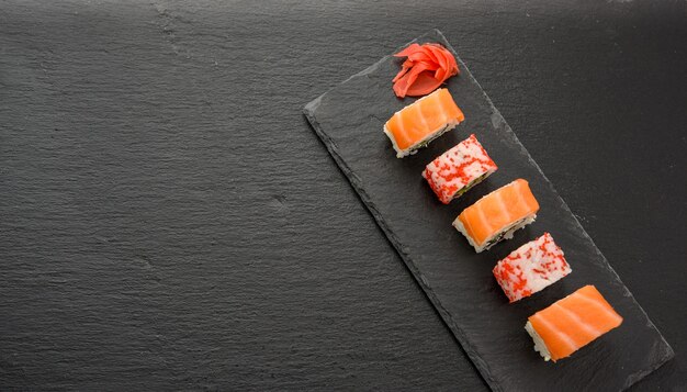 Kalifornien-Sushi mit rotem Tobiko-Kaviar und Scheiben von Philadelphia-Sushi auf schwarzem Schieferbrett, Draufsicht