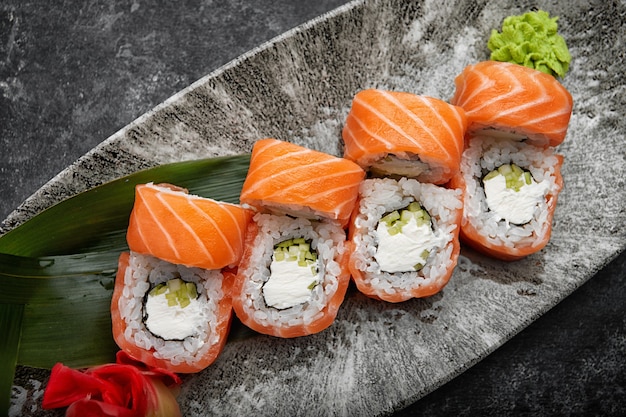 Kalifornische Sushi-Rolle mit Gurken-Avocado-Frischkäse und Lachs auf einem grauen Teller auf einem dunklen Tisch