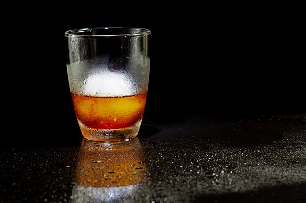 Kalte Americano-Dekoration mit Eisball im Whiskyglas auf einem schwarzen Tisch.