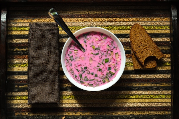 Kalte Rote-Bete-Suppe auf einem Löffel in der Hand und Brot auf einem dekorativen Tablett