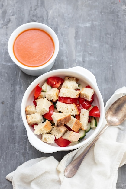 Kalte Tomatensuppe Gaspacho mit Brot in der weißen Schüssel auf keramischem Hintergrund