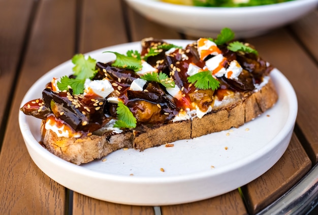 Kalte Vorspeise aus gebratenen Auberginen in einer süßen Sauce, dekoriert mit frischen Kräutern mit Mozzarella-Käsestücken, bestreut mit Knjutsamen.