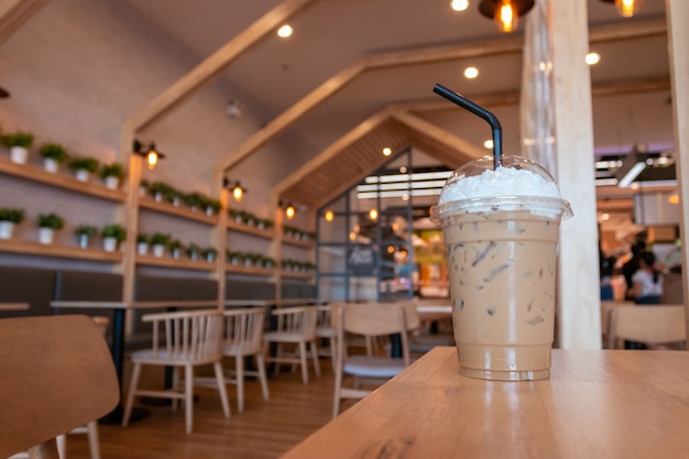 Kalter Cappuccino mit Schlagsahne in der Tasse zum Mitnehmen auf Holztisch im Café-Hintergrund.