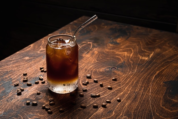 Kalter Espresso Tonic Ein Longdrinkglas gefüllt mit Eiswürfeln Tonic Sodawasser Kaffeebohnen um Holzhintergrund