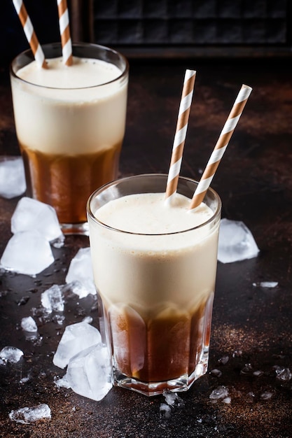 Kalter Frappe-Kaffee mit Eis und Schaum in großen Gläsern auf selektivem Fokus des braunen Hintergrundes