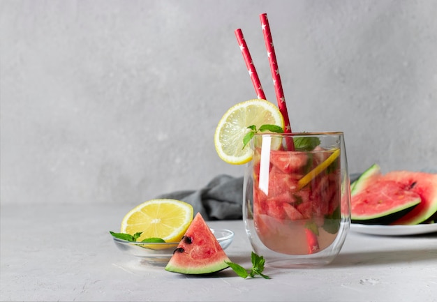 Kalter heller Wassermelonen-Mojito-Cocktail mit tadellosen Zitronenscheiben und Trinkhalm auf grauem Hintergrund