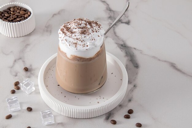 Kalter Kaffee mit Schokoladenmilch und Eis mit Schlagsahne und Zimt in einem Glasglas auf einem Marmortisch kaltes Sommerdessert