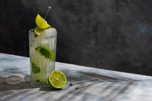 Kalter Mojito-Cocktail mit Rum-Limetten-Eiswürfeln und Minze Tropischer Palmblattschatten