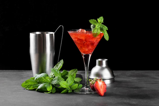 Kalter Sommer-Erdbeer-Cocktail Mojito Margarita Daiquiri in einem Martini-Glas auf dunklem Hintergrund mit Barkeeper-Set