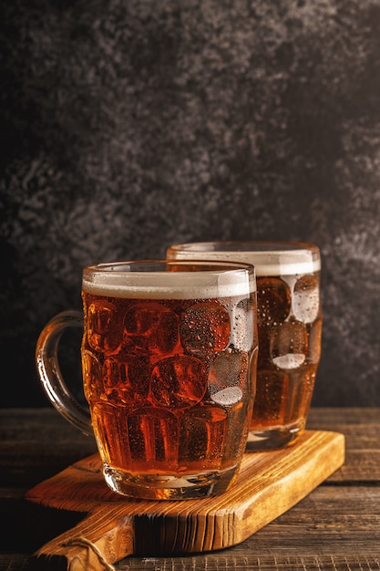 Kaltes Bier im Glas mit Pommes auf einem dunklen Tisch.