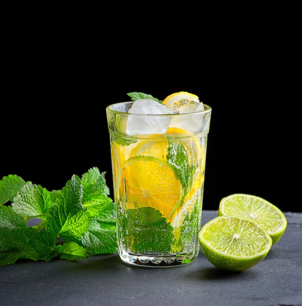 Kaltes Getränk aus Zitronenstücken, Limetten und Blättern der grünen Minze in einem Glas mit Wassertropfen