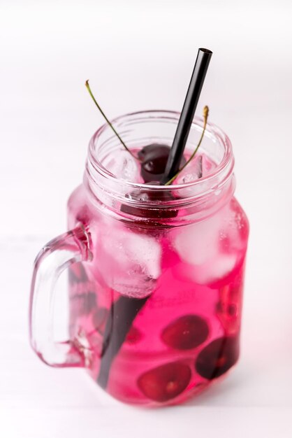 Kaltes Getränk mit Kirsche in Gläsern auf weißem Holzhintergrund Sommergetränk mit kaltem Detox-Wasser