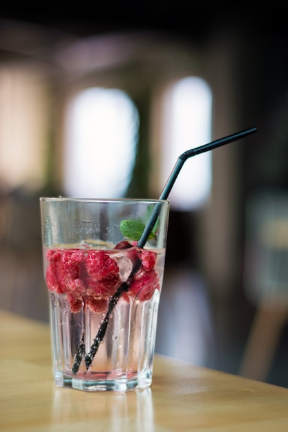 Kaltes Himbeergetränk mit tadellosen Blättern in einem verschwitzten Glas auf einer Tabelle in einem Café