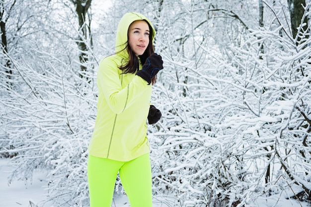 Kaltes Wetter läuft glückliche Frau, die im verschneiten Parkwald des Winters läuft Sportlerin sprintet