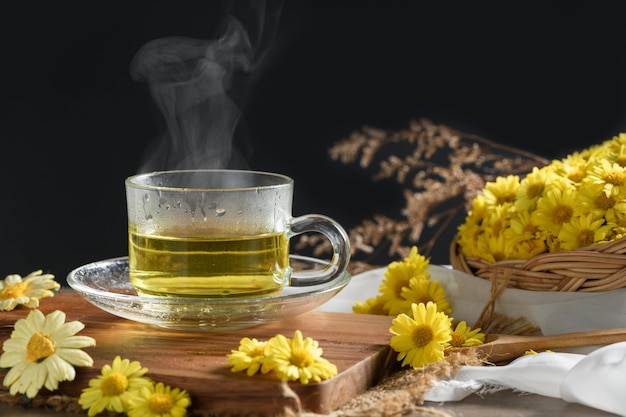 Kamillentee mit heißem Dampf und Kamillenblume im Korb auf Schwarz. Gesundes Getränk zum Trinken. Kräuter und medizinisches Konzept.