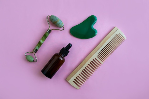 Kamm und Flasche für Kosmetika aus Jade-Massagegeräten auf rosa Hintergrund Hintergrund mit Kopierraum