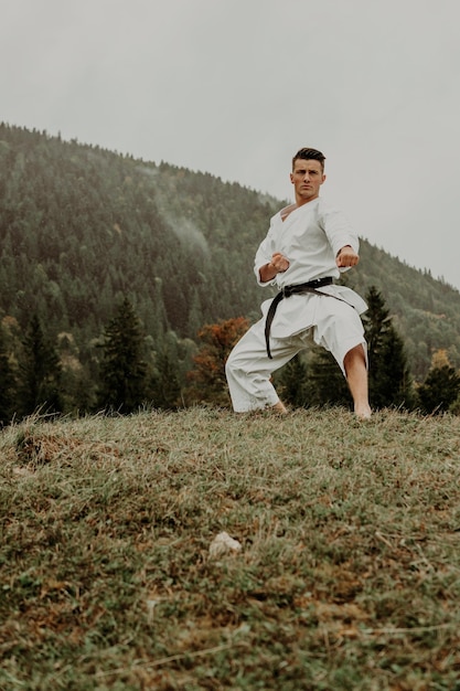 Kampfkunst Karate ein Mann im Kimono mit schwarzem Gürtel trainiert auf dem bergfreien Raum