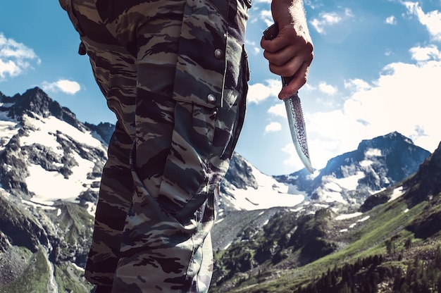 Kampfmesser in der Hand der Soldat das Kommando im Hintergrund der schneebedeckten Gipfel in den Bergen. Scout mit einem Messer. Touristischer Rucksacktourist hält das Messer in freier Wildbahn.