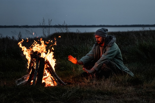 Kampierender Mann, der nachts am Feuer gegen den Himmel sitzt. Reisen, Tourismus, Camping.