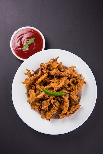 Kanda bhaji crujiente o Bhajji o Pyaj Pakode o pakora de cebolla frita, deliciosa comida callejera, bocadillo indio favorito en el monzón servido con salsa de tomate y té caliente