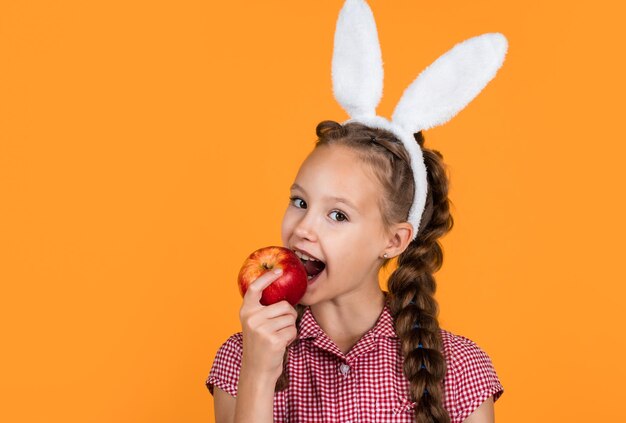 Foto kaninchen-mädchen beißt in den roten apfel, bereit für die eierjagd. glückliches ostern.