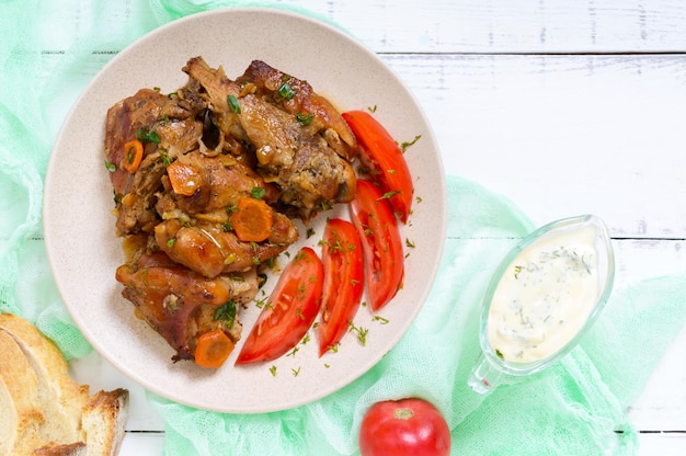 Kaninchenstücke mit Tomate, Soße und Grüns auf einem weißen hölzernen Hintergrund. Ansicht von oben.