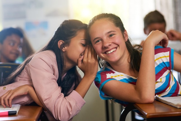 Kannst du ein Geheimnis bewahren Aufnahme eines jungen Schulmädchens, das ihrer Freundin in der Klasse ein Geheimnis zuflüstert